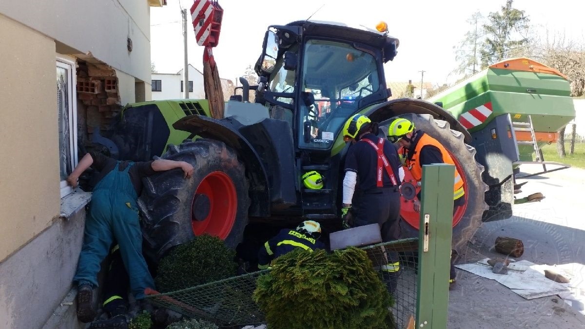 PAK_DN_Traktorista smetl ženu, která zůstala zaklíněná pod traktorem_hasičI vyprošťujÍ ženu_pohled na traktor a rozbitý dům.jpg