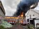SČK_Požár haly s uskladněným senem v Bartošovicích_2 hasičské vozy stojí před hořící halou, ze které šlehají plameny a černý dým_4 hasiči v akci