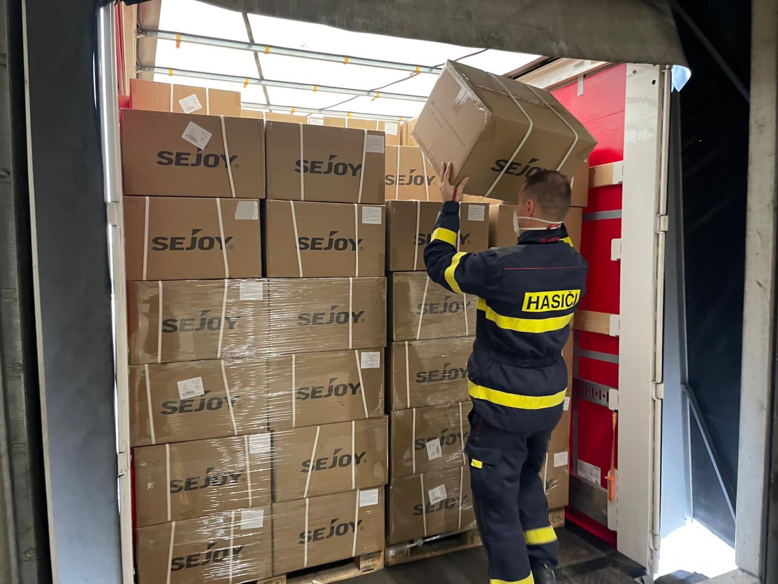 Příslušník ZÚ HZS ČR nakládá krabice s respirátory na korbu nákladního vozu .jpeg