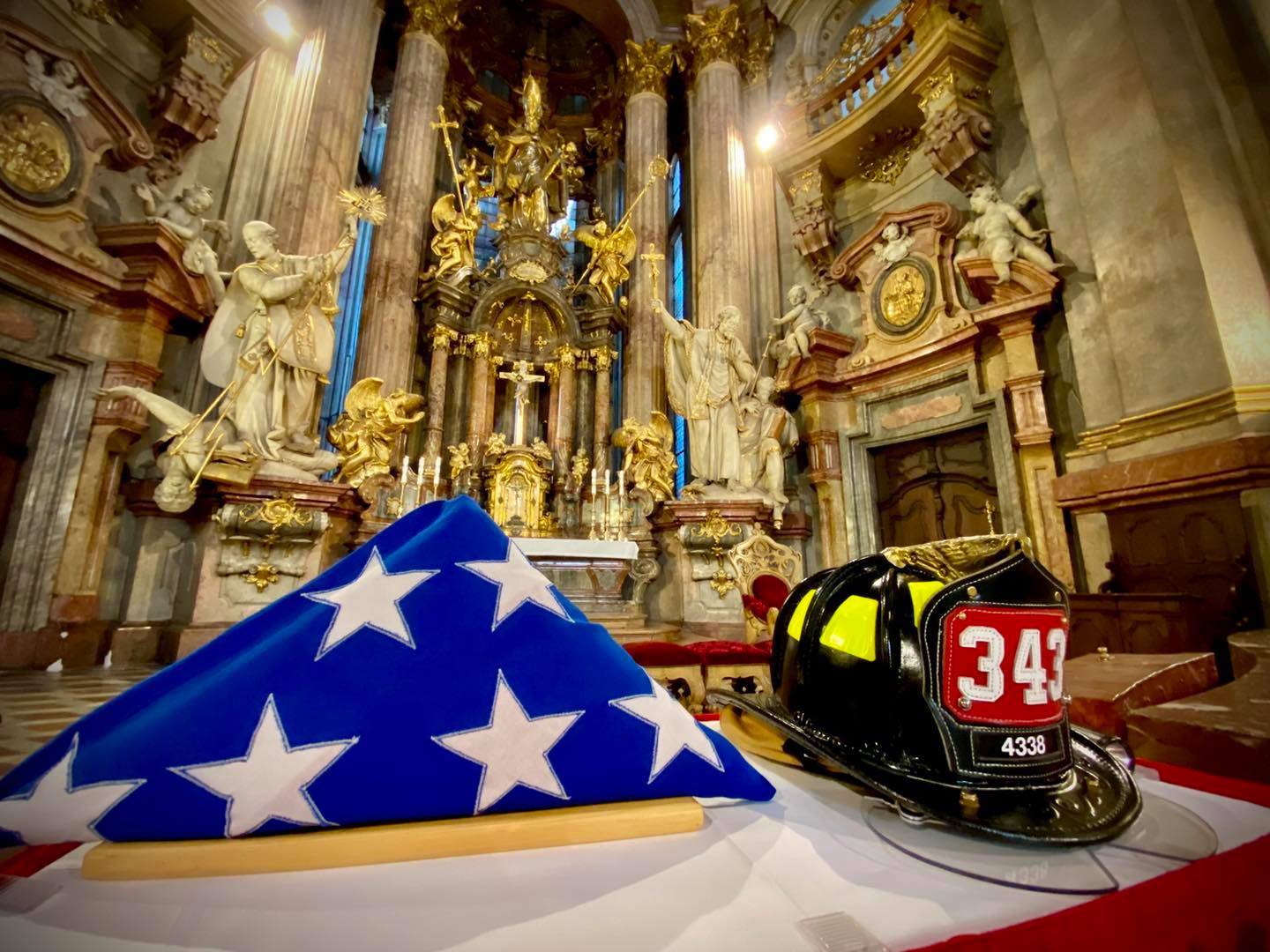 Pietní akt v chrámu sv. Mikuláše, pohled na přilbu amerického hasiče a americkou vlajku před oltářem.jpg