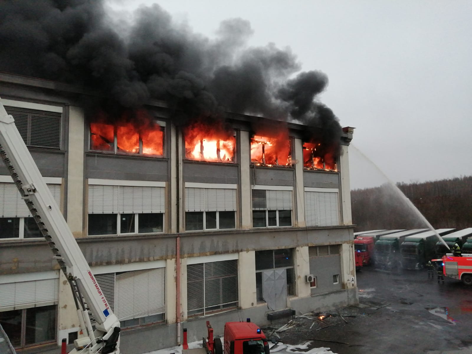 ÚLK_požár haly s plastovými modely v Mostě_pohled na hořící 2. patro haly a hasiče hasící pomocí CAS.jpg
