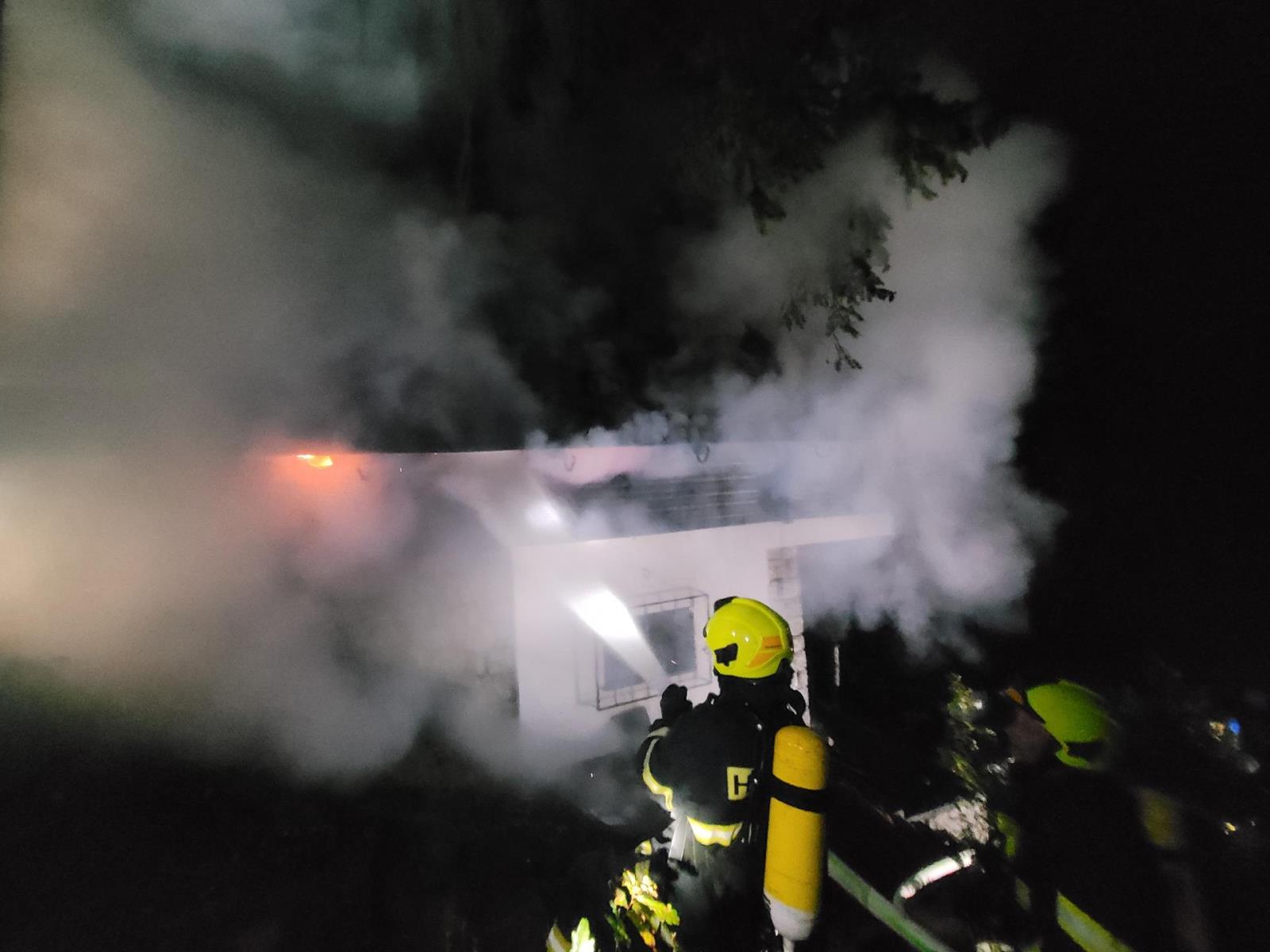 SČK_Požár chaty v Kamenném Přívozu_hasiči hasí hořící budovu z venku.jpg