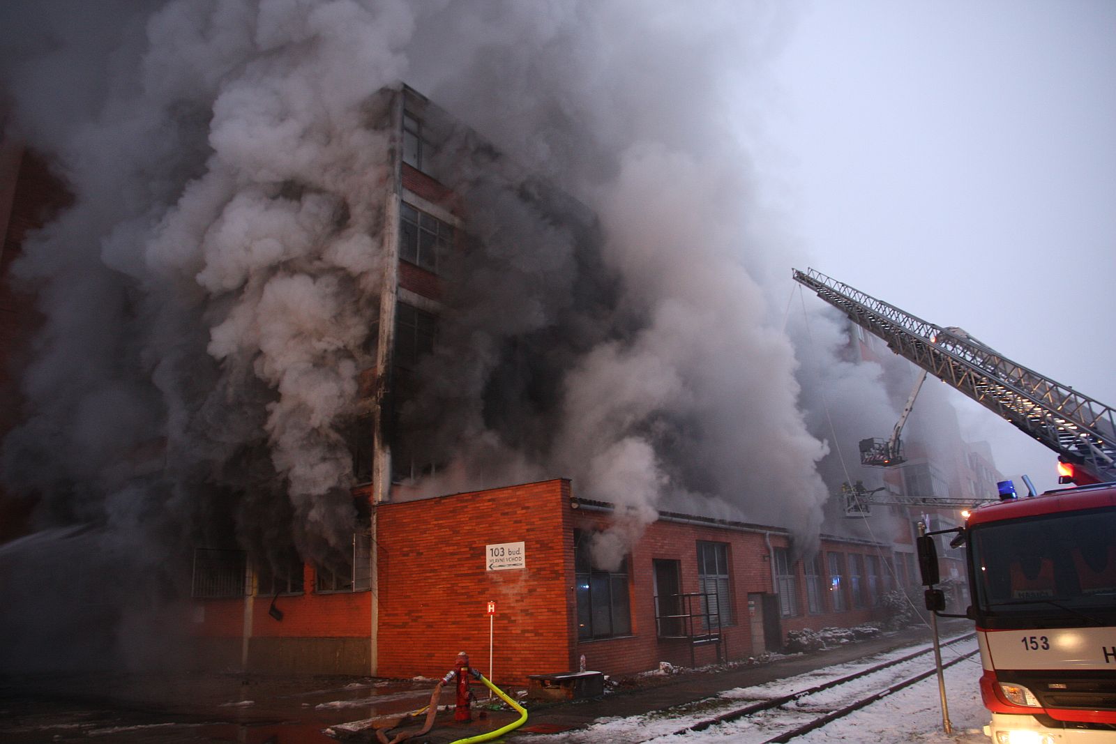 3_ZLK_požár Svit Zlín_hustý kouř stoupá z budovy_v popředí stojí has. autem s vysunutým žebříkem.jpg